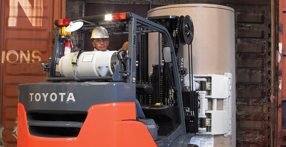 Man safely reversing a Toyota forklift while carrying a large cylinder container in a warehouse 